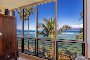Una habitación con ventanas amplias que ofrecen vista al océano y palmeras.
