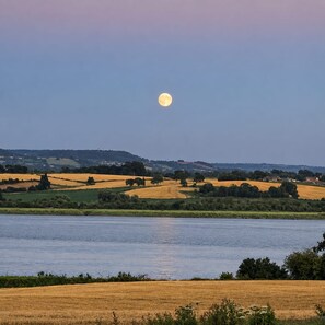 A landscape with a body of water, fields, and a moon in the sky. - The Riverside Retreat (GLOUCESTERSHIRE)