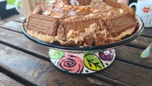 A cake with chocolate and caramel layers on a stand with a colorful base. - The Riverside Retreat (GLOUCESTERSHIRE)