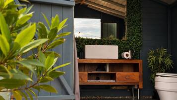 A modern outdoor bathroom with a built-in sink, wooden vanity, and a green vertical garden.