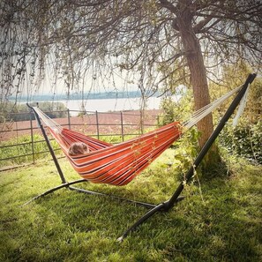 A hammock tied between two trees, overlooking a grassy area with a view of a body of water and distant landscape. - The Riverside Retreat (GLOUCESTERSHIRE)