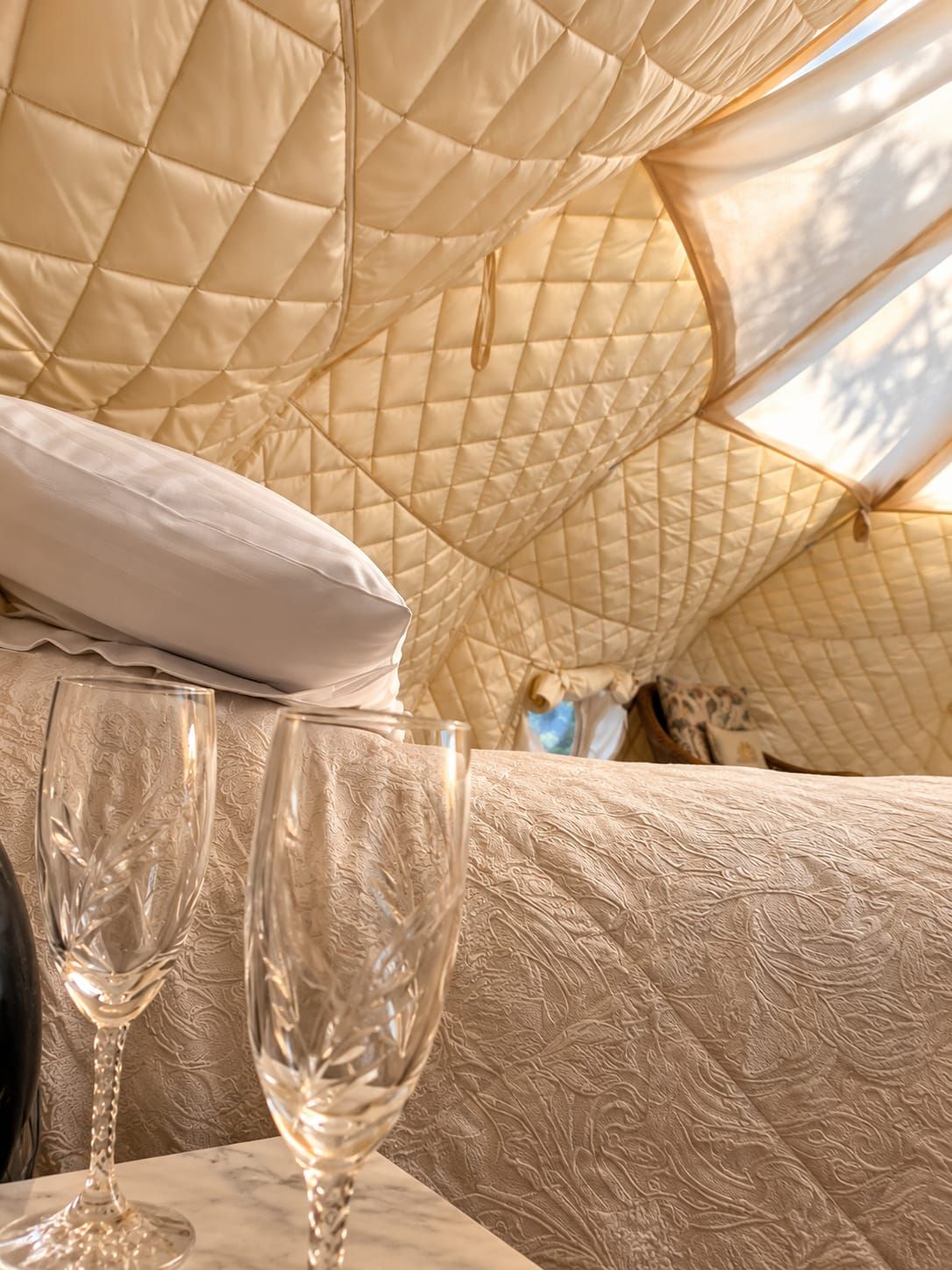 Une tente aménagée avec un intérieur matelassé, un oreiller blanc et deux verres à vin vides posés sur une table.