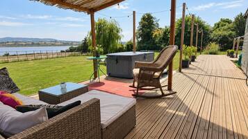 A wooden deck with outdoor furniture, a hot tub, and a view of a lake.