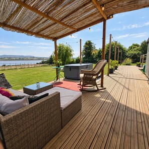 Una terraza de madera con mobiliario exterior, un jacuzzi y vistas a un lago.
