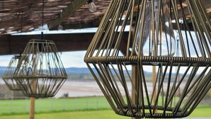 A series of hexagonal wicker light fixtures suspended from a wooden structure, likely part of an outdoor seating area with a view of a body of water and greenery in the background. - The Riverside Retreat (GLOUCESTERSHIRE)