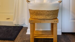 A bathroom with a wooden stool holding a basket of towels, a shower curtain, and framed pictures on the wall. - Beautiful New 4-BR Home Near All Major Attractions (Palm Coast)