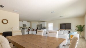 A spacious living room with a large wooden dining table, white sofas, and a TV. - Beautiful New 4-BR Home Near All Major Attractions (Palm Coast)