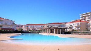 Ein Schwimmbecken, umgeben von mehrstöckigen Gebäuden mit Balkonen, einer überdachten Sitzgelegenheit und blauem Himmel.