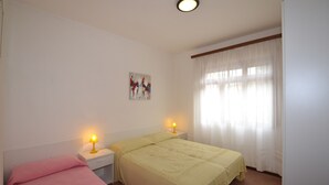 A bedroom with two beds, a nightstand with lamps, a painting on the wall, and a window with sheer curtains. - Comfortable and Bright Flat - Beahost (San Michele al Tagliamento)