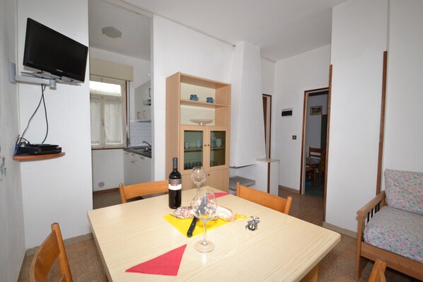 A dining area with a table set for two, a wine bottle, and a glass. There is a wooden cabinet with dishes and a television mounted on the wall. - Comfortable and Bright Flat - Beahost (San Michele al Tagliamento)