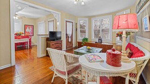 A living room with a television, wicker furniture, a red lamp, and a dining area with a red table and chairs.