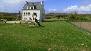 Une maison blanche avec un toit en pente, une balançoire en bois et une cour couverte d’herbe.