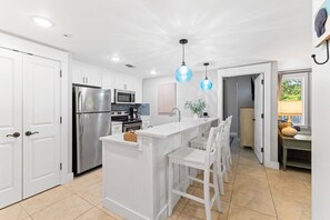 A modern kitchen with white cabinetry, stainless steel appliances, a central island with bar stools, and pendant lighting.