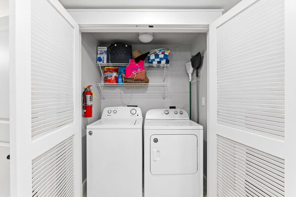 A laundry room with two front-loading washers, a shelf with cleaning supplies, and a fire extinguisher. - Baytowne Wharf Condo-Large Private Balcony-Beach (Miramar Beach)