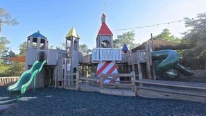 Un parque infantil con un tobogán, estructuras para escalar y una casita de juegos.