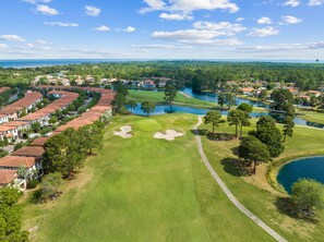 Ein Golfplatz mit Sandbunkern, einem Wasserhindernis und Wohnhäusern.