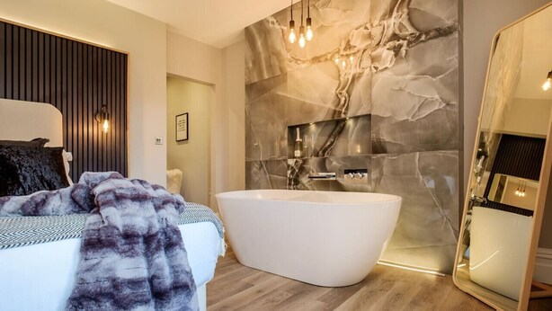 Ein modernes Badezimmer mit freistehender Badewanne, einem großen Spiegel und einer Marmorwand.