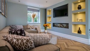 Ein modernes Wohnzimmer mit einer Sofagarnitur, einem flachbildfernseher an der Wand und einer eingebauten Regalanlage mit Dekorationselementen.