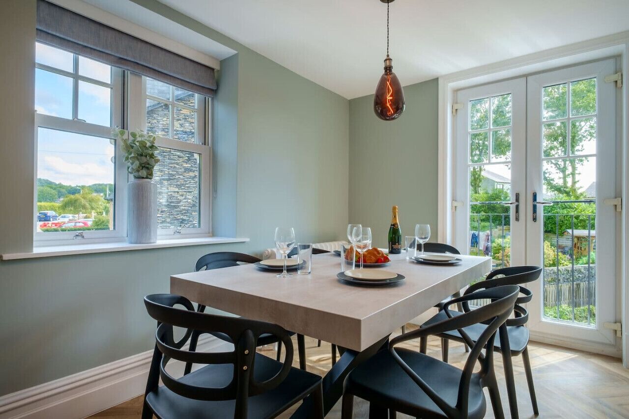 A dining area with a table set for four, a hanging light fixture, and a view through a window.