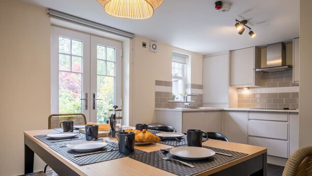 A modern kitchen with white cabinets, a black countertop, and a window overlooking a garden. - Leven  The  Bowering (Cumbria)