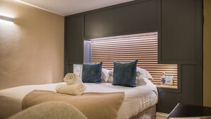 A neatly made bed with pillows, a bedside table with a bottle and a box, and a wall-mounted shelf. - Leven  The  Bowering (Cumbria)