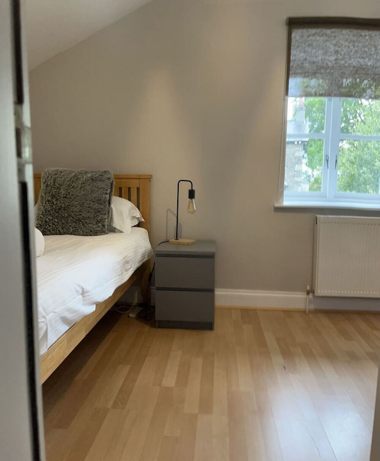Une chambre à coucher avec un lit, une table de chevet avec une lampe, une fenêtre et un radiateur.