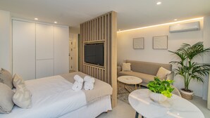Ein modernes Hotelzimmer mit Bett, einer Couch, einem runden Couchtisch und einer Zimmerpflanze.