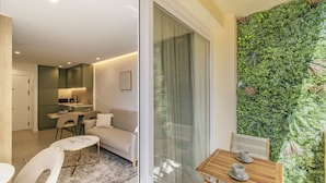 Ein modernes Wohnzimmer mit Sofa, Couchtisch und Sesseln, ein Küchenbereich mit Esstisch und eine grüne vertikale Wand.