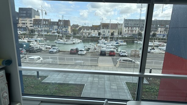 A view from a room with a large window overlooking a marina with boats and cars.