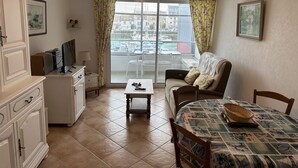 A compact living room with a sofa, a small table, a TV, and a balcony with a view of the city.