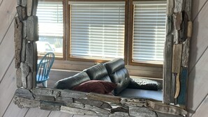 A rustic mirror with a stone frame reflecting a room with a leather sofa and a window with blinds. - Ocean view guest suite, completely self contained, beautiful outdoor patio (Campbell River)