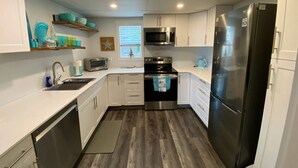 A compact kitchen with white cabinets, stainless steel appliances, and a wooden floor. - Ocean view guest suite, completely self contained, beautiful outdoor patio (Campbell River)