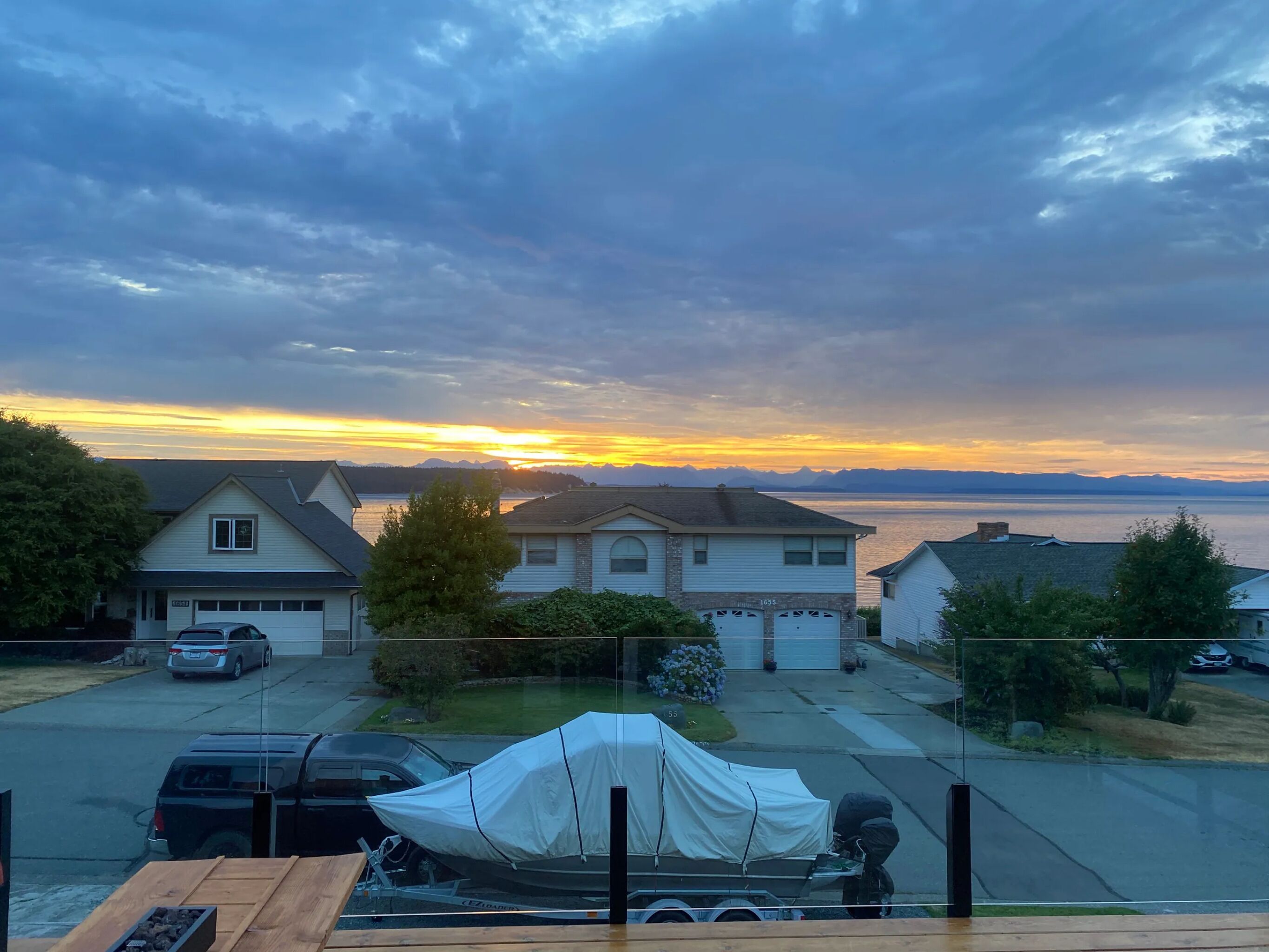 A residential area with houses, a covered boat, and a view of the sunset over a body of water.