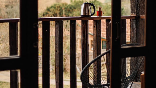 A wooden deck with a chair and a table, a view of a hilly landscape, and a window frame. - Refúgio dos pinhais (Sapucai-Mirim)