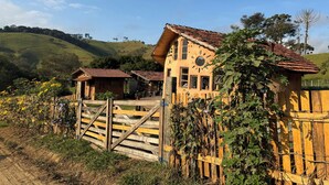 A rustic house with a tiled roof, surrounded by a wooden fence and overgrown with vines. - Refúgio dos pinhais (Sapucai-Mirim)