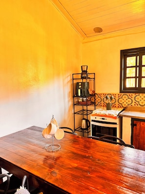 A kitchen with a wooden table, a coffee machine, a stove, and a window with a view. - Refúgio dos pinhais (Sapucai-Mirim)