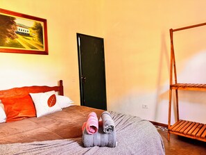 A bedroom with a bed, pillows, a painting, a door, and a wooden shelf. - Refúgio dos pinhais (Sapucai-Mirim)