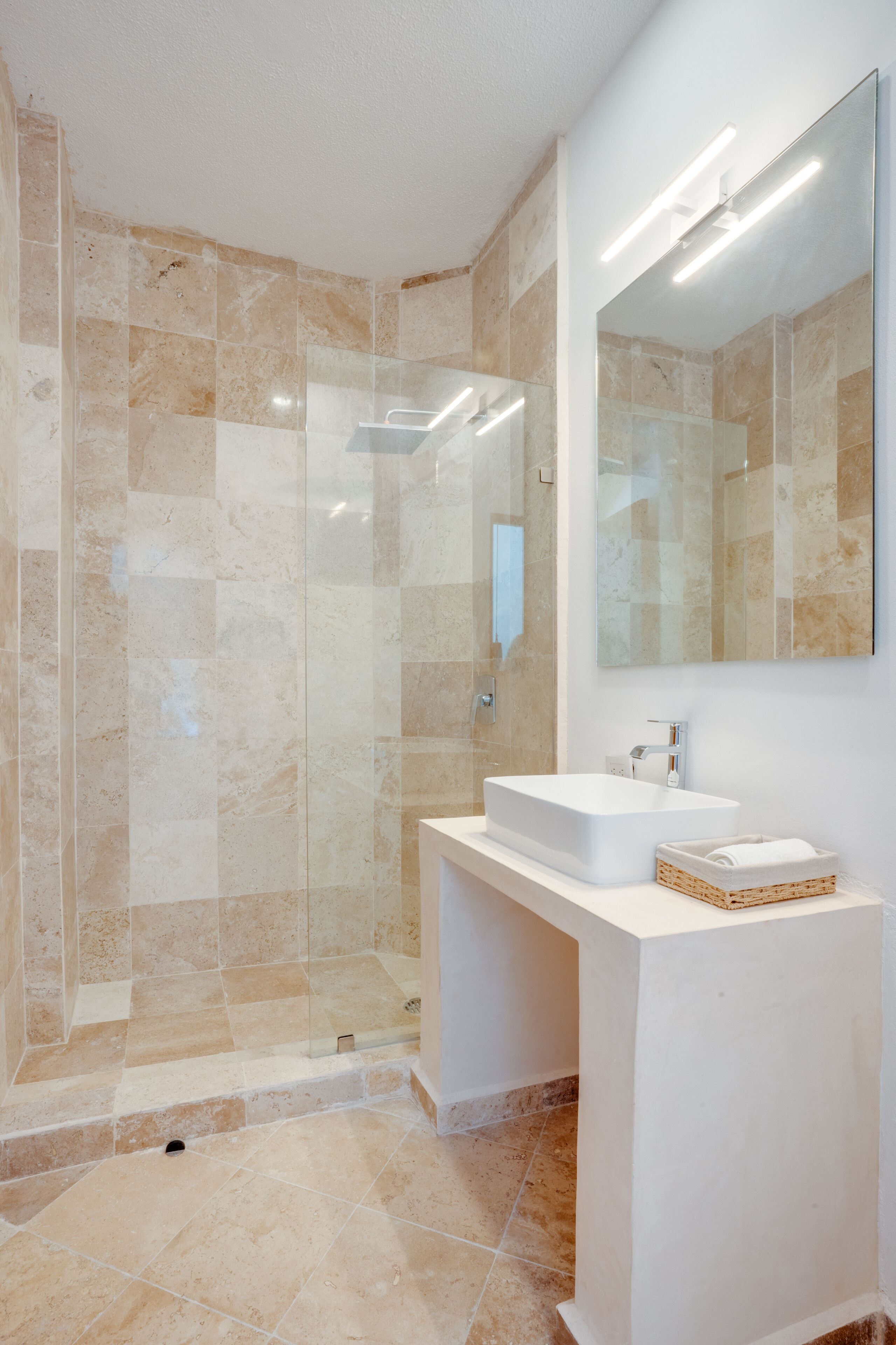 Un baño moderno con ducha envuelta en vidrio, un lavabo blanco y un espejo grande.