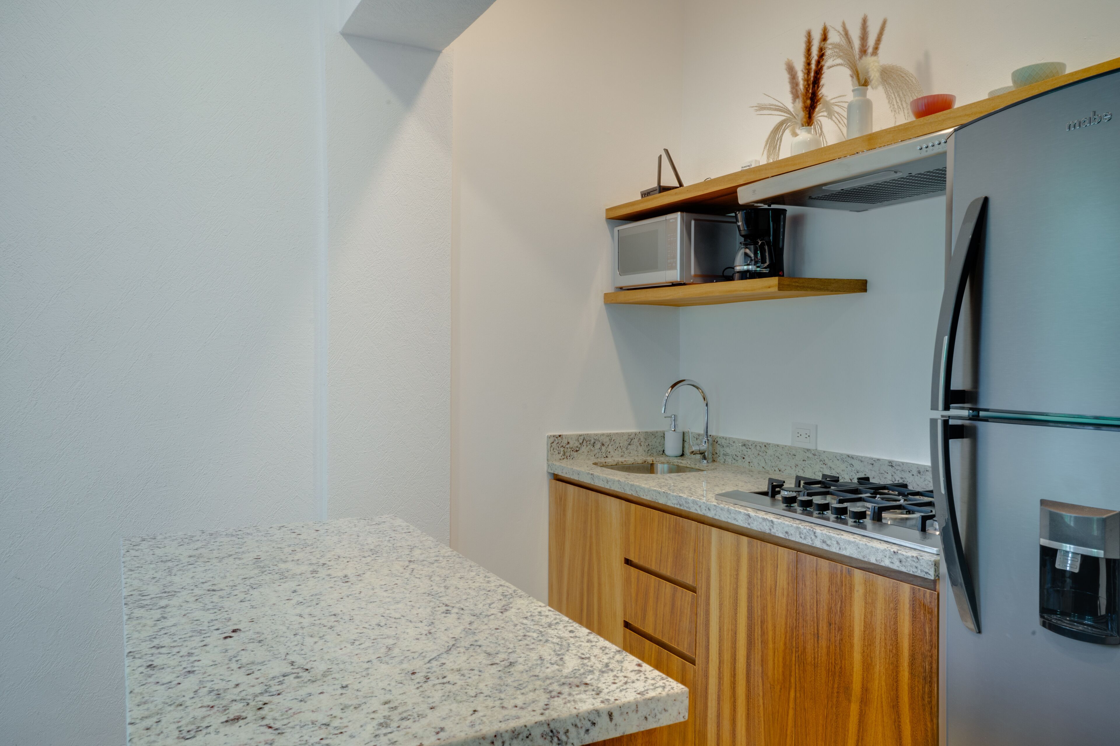 A modern kitchen with granite countertops, wooden cabinets, a stainless steel refrigerator, a microwave, and a gas stove.