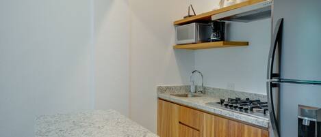 A modern kitchen with granite countertops, wooden cabinets, a stainless steel refrigerator, a microwave, and a gas stove.