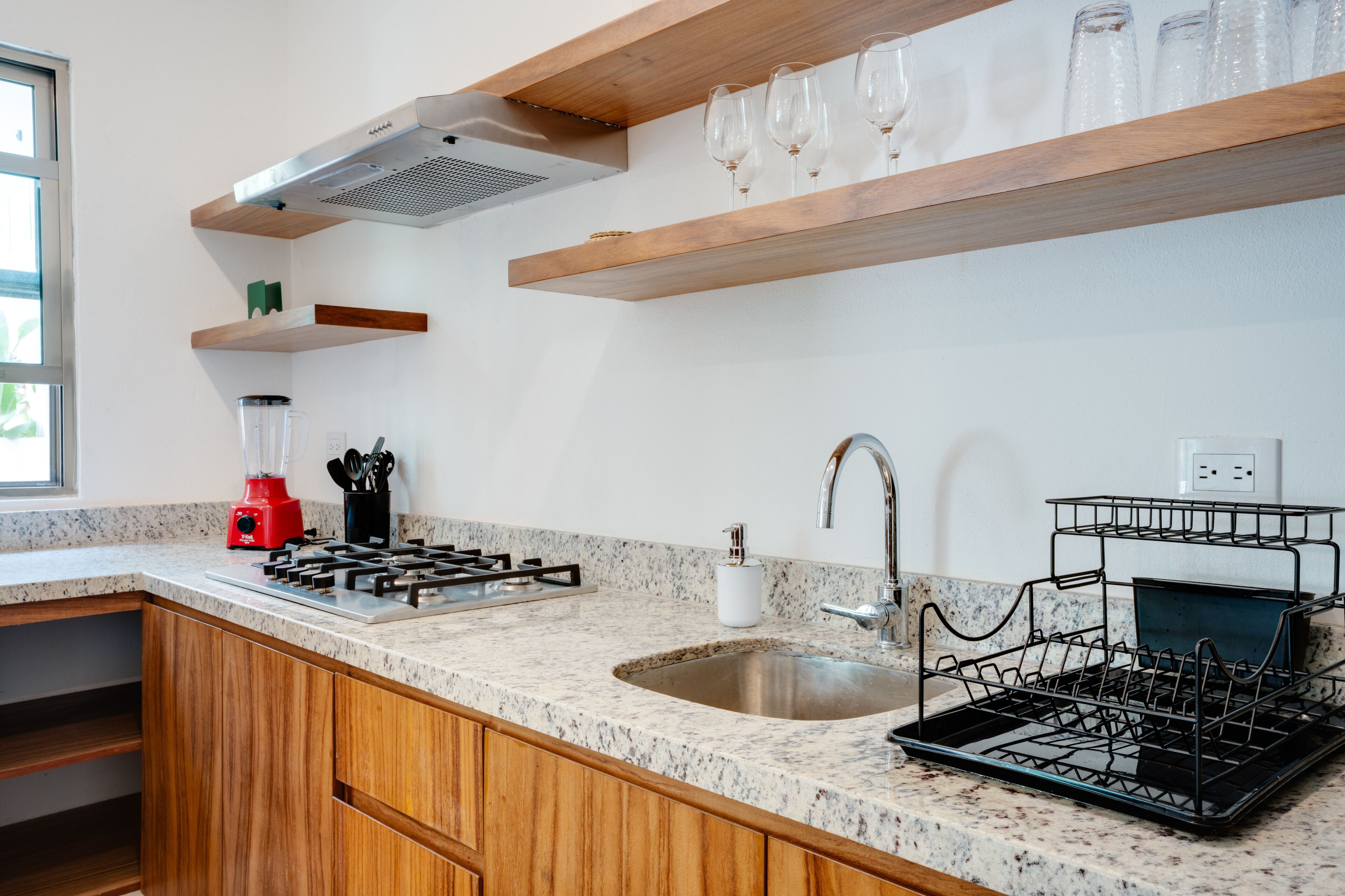 Une cuisine dotée d’un plan de travail en granit, de meubles en bois, d’une cuisinière à gaz, d’un évier et d’un égouttoir à vaisselle.