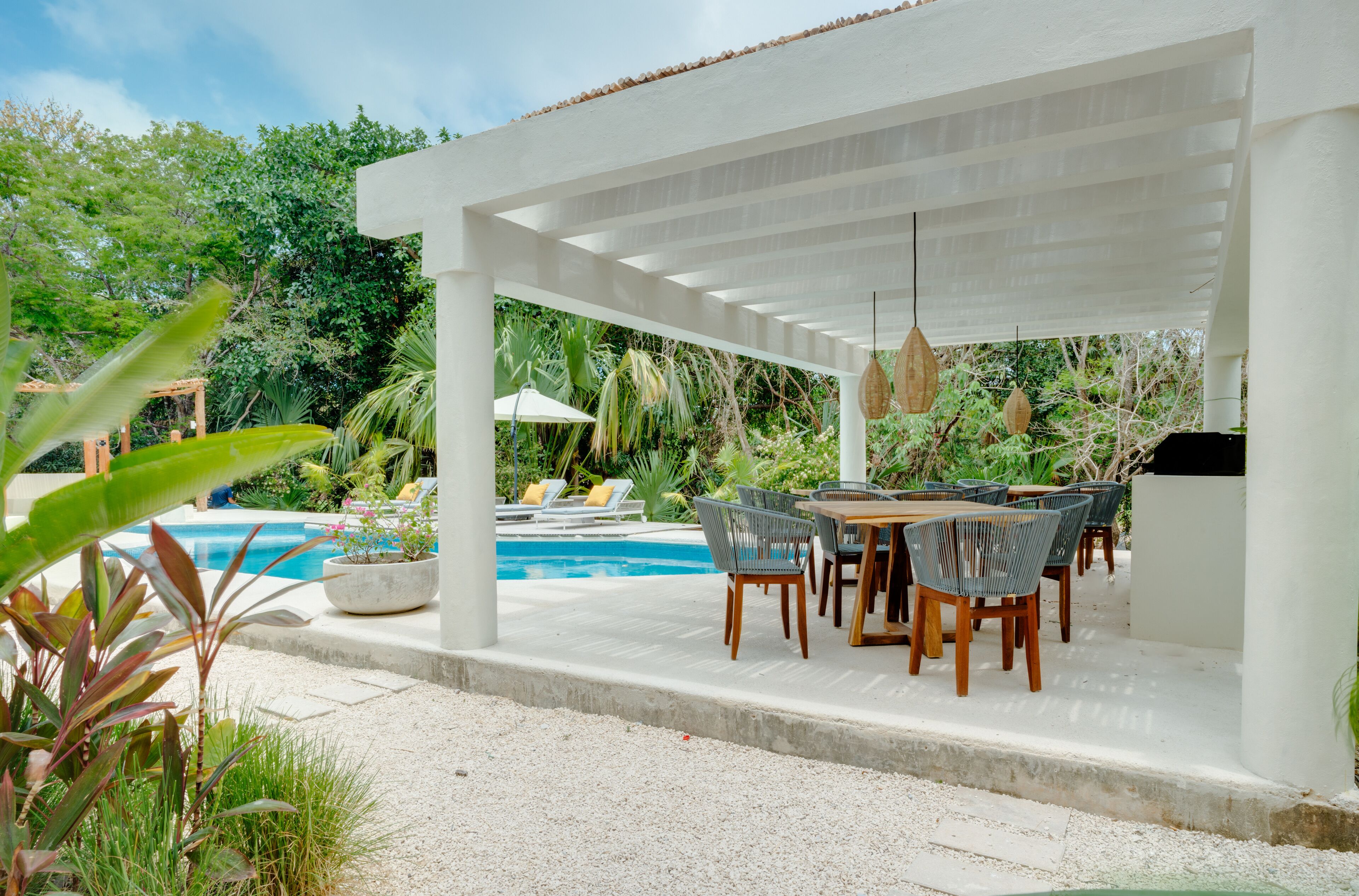 A covered outdoor area with a pool, lounge chairs, and a dining setup.