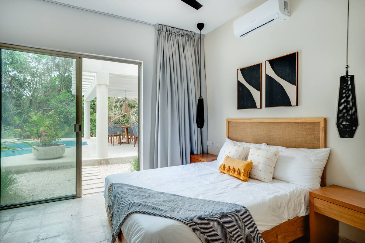 Un dormitorio moderno con una cama grande, cabecera de madera y vistas a una piscina y zona exterior.