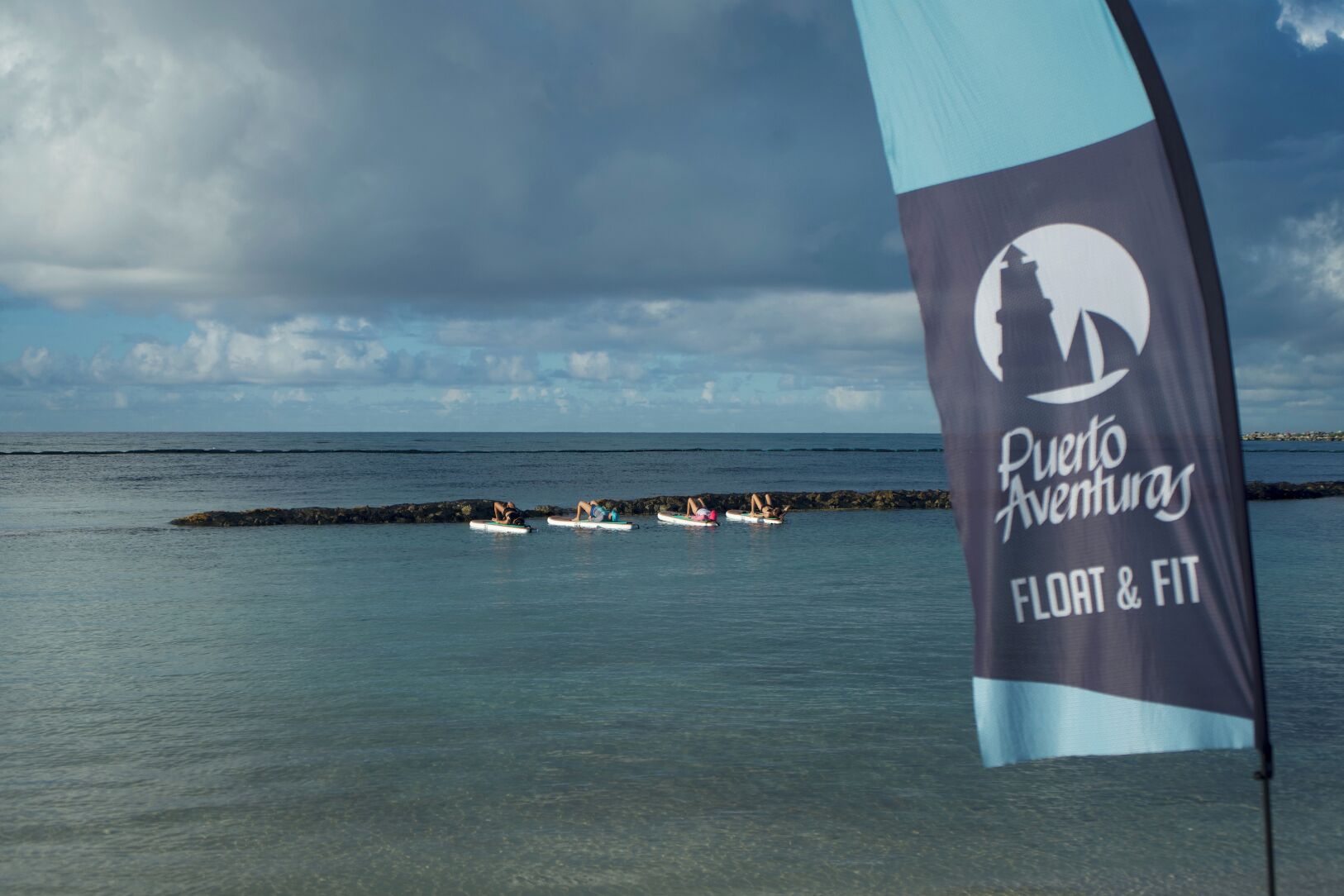 A beach scene with a flag reading "Puerto Aventuras Float & Fit".
