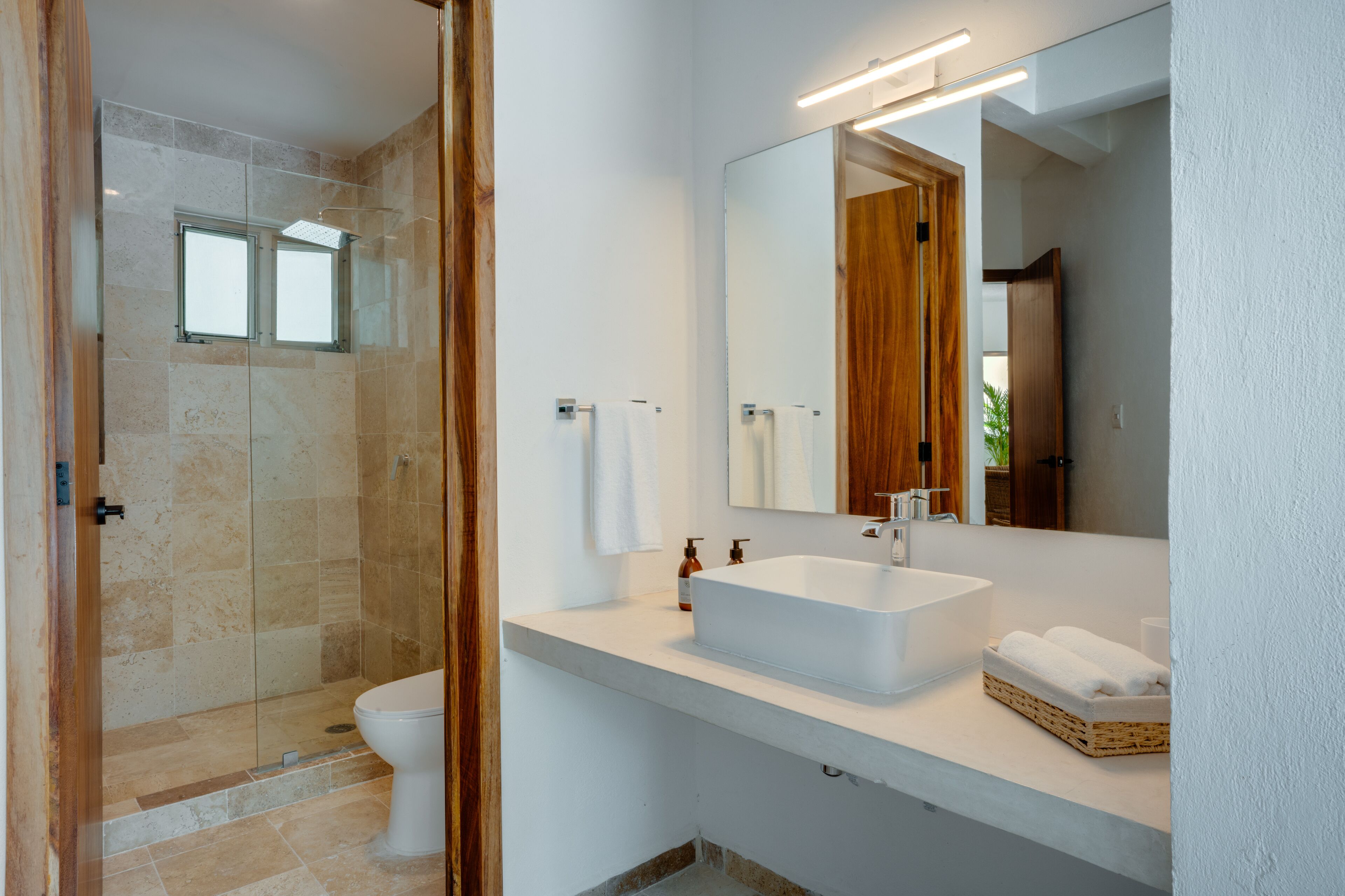 A modern bathroom with a large mirror, a white sink, and a glass-enclosed shower.