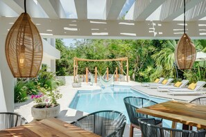 A poolside area with a wooden table and chairs, a hammock, and lounge chairs. - Casa Manglar Riviera Maya (Puerto Aventuras)