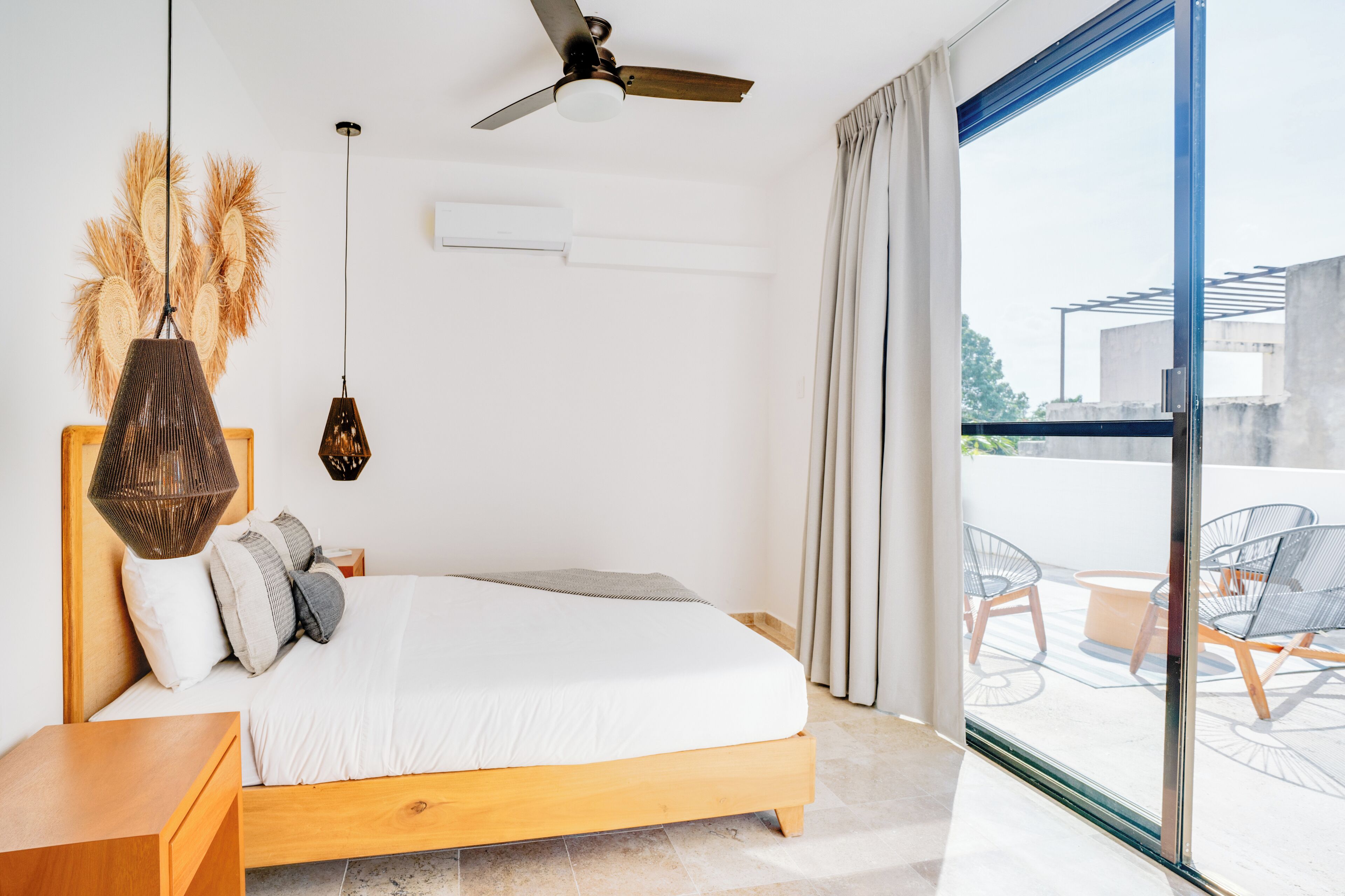 A modern bedroom with a wooden bed, a ceiling fan, and a large window offering a view of the outdoors.