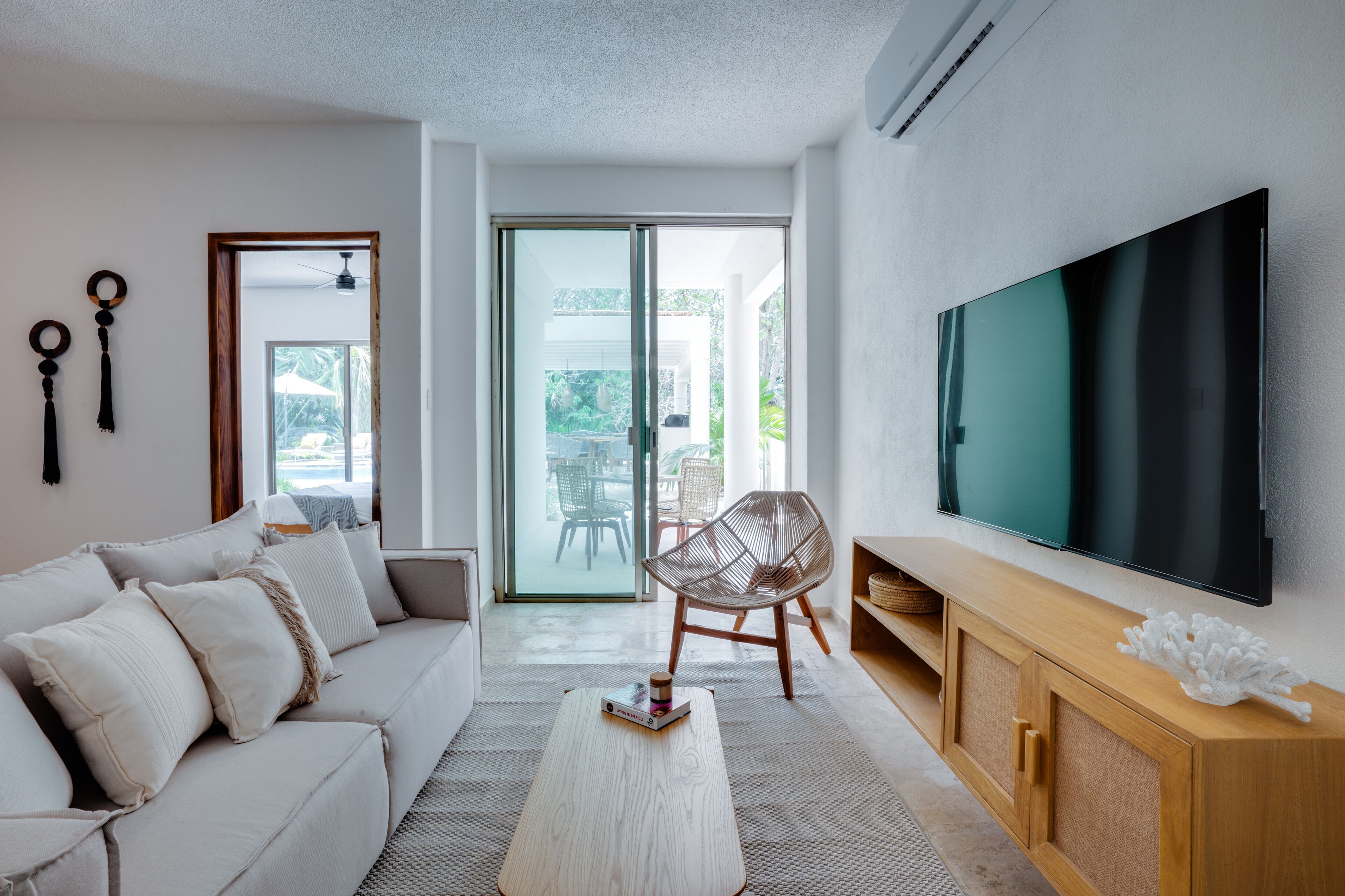 Un salón moderno con un sofá, una mesa de centro, un televisor y un ventanal corredera que da a un espacio exterior.