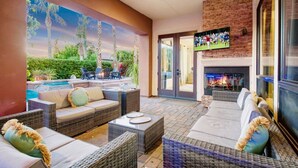 A cozy outdoor seating area with wicker furniture, a fireplace, and a television screen. - Arcade Blast/Pool/Spa/100k Game Room (Indio)