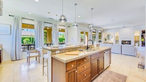 A spacious kitchen with a large island, pendant lights, and a view of greenery outside. - Arcade Blast/Pool/Spa/100k Game Room (Indio)